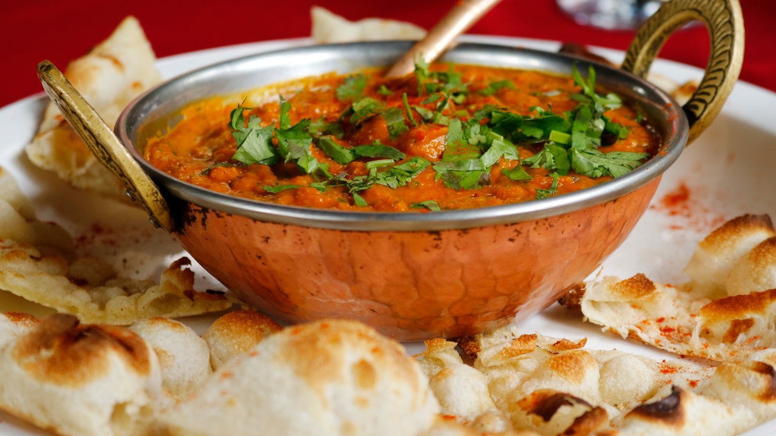 Mangkuk butter chicken saus oranye creamy dengan potongan ayam dan taburan krim putih