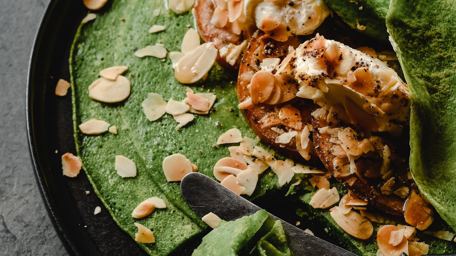 Gulungan crepe hijau pandan berisi krim manis ditata di piring datar