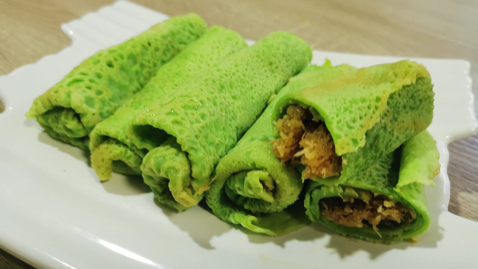 Dadar gulung: crepe pandan hijau berisi unti kelapa gula merah, sebagian terlihat isinya