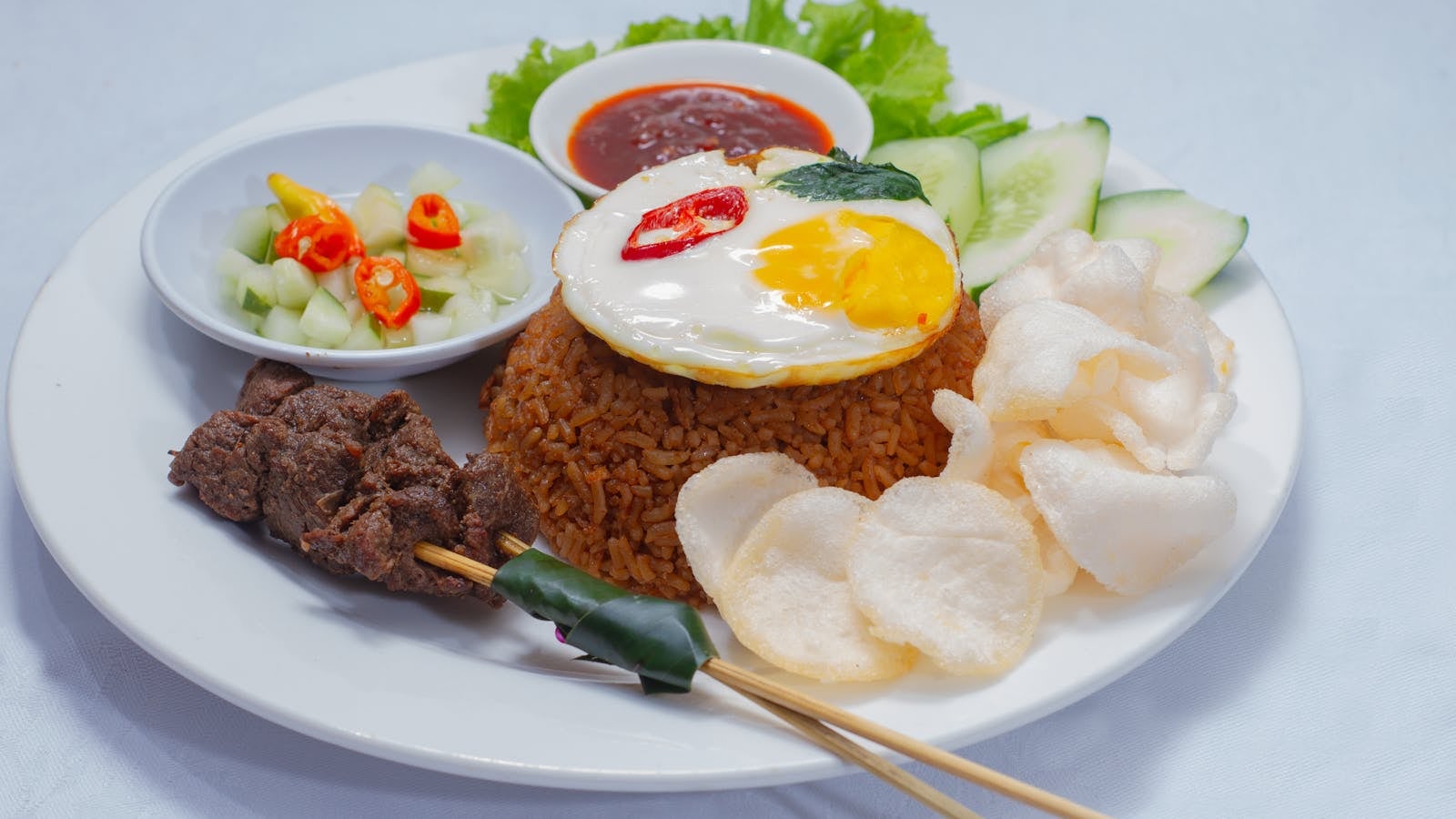 Nasi goreng kampung dengan telur ceplok, sate, dan kerupuk di piring