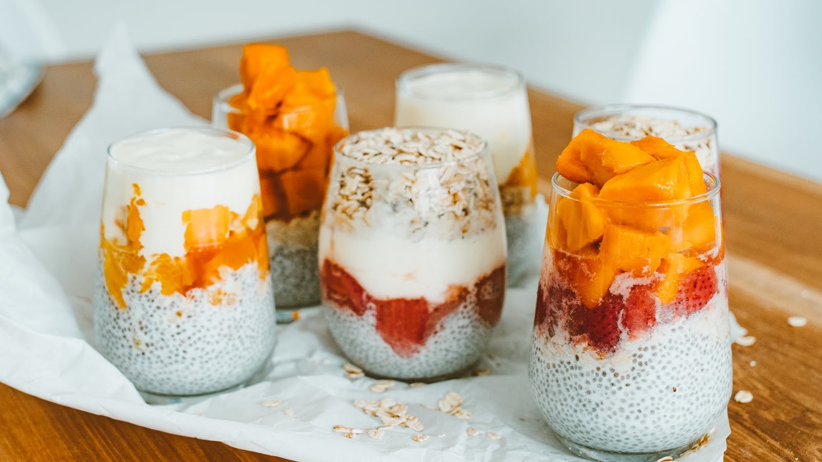 Lima jar overnight oats dengan topping mangga, blueberry, dan kacang almond ditata berjajar