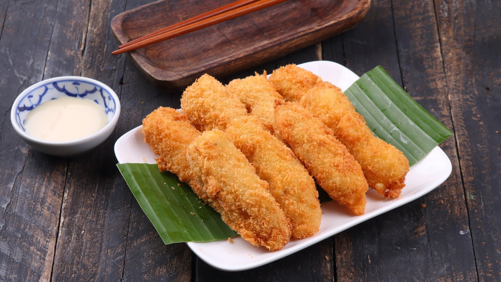 Pisang goreng crispy keemasan dengan saus cocolan di piring