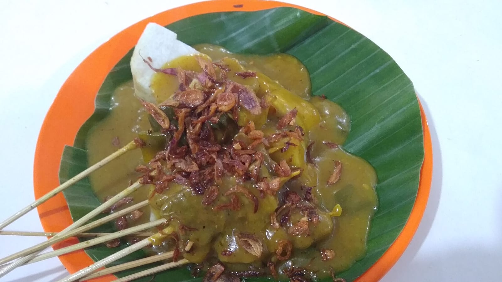Sate Padang: sate daging disiram kuah kuning kental dan bawang goreng, dengan ketupat