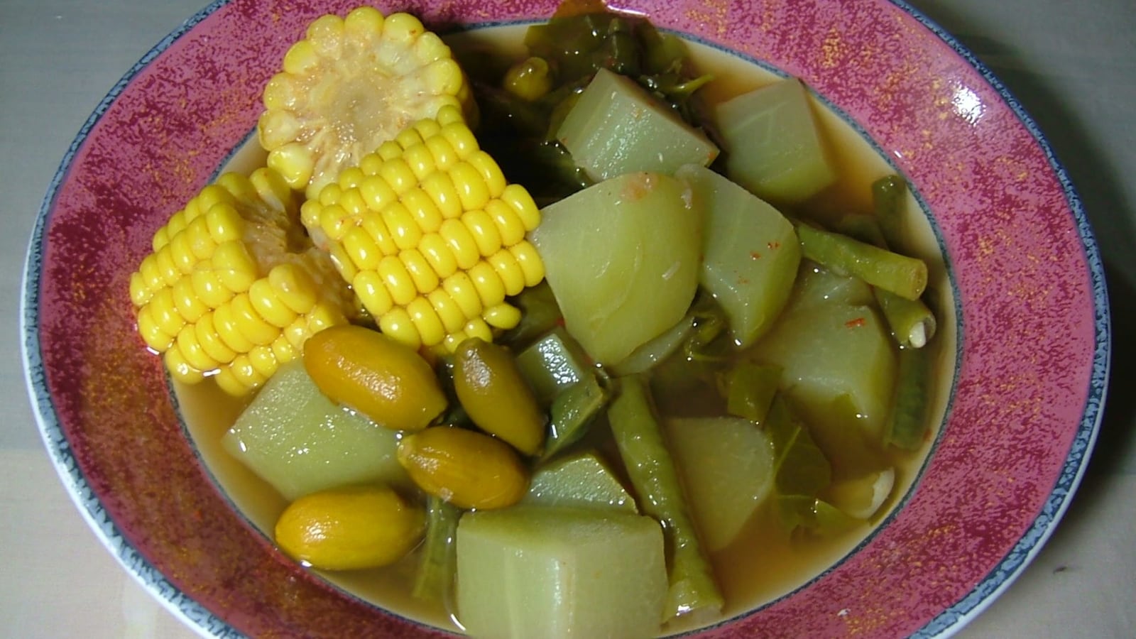 Sayur asem dengan kuah asam jernih, jagung manis, labu siam, kacang panjang, dan biji melinjo di piring keramik