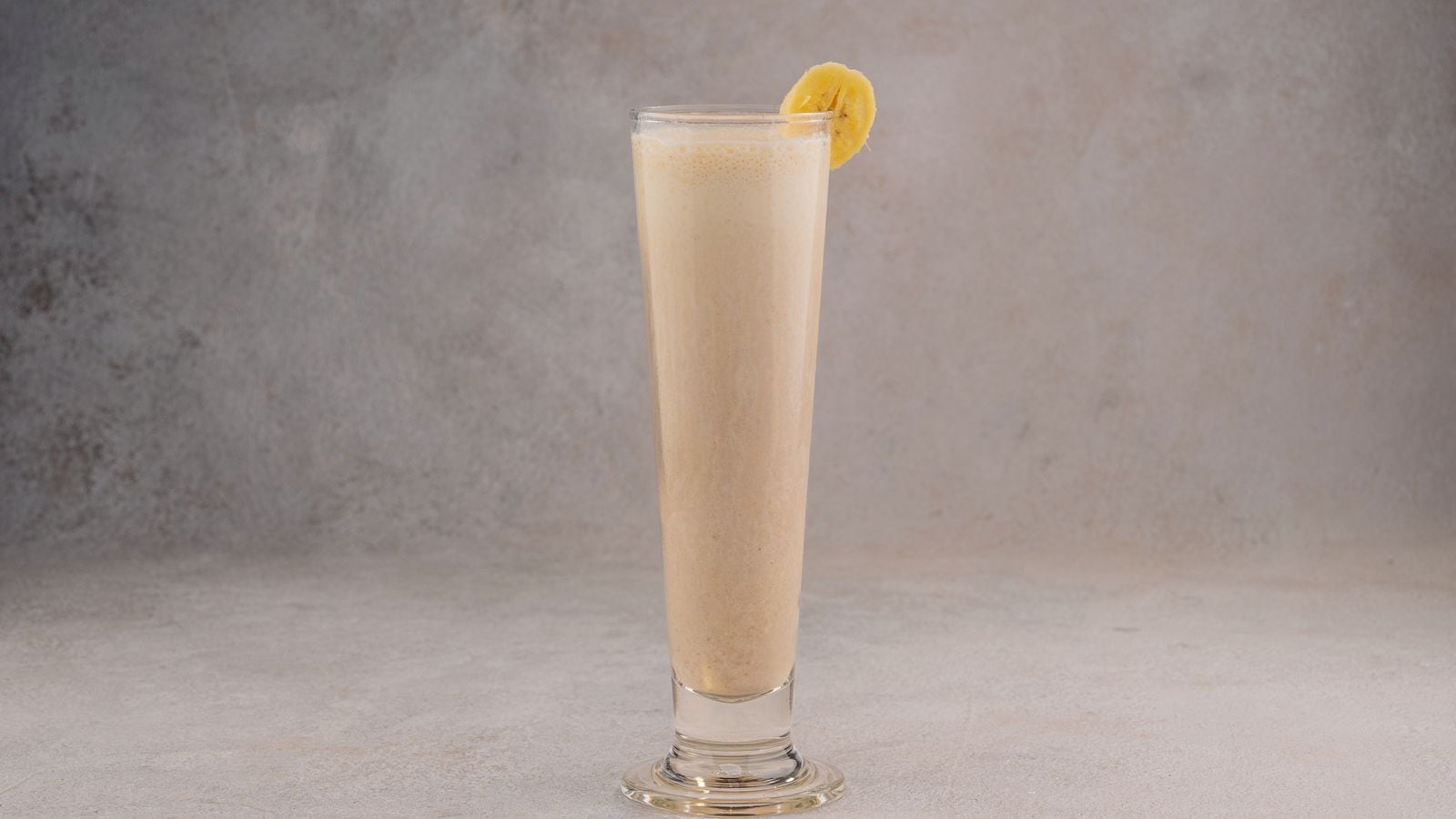 Smoothie pisang creamy di gelas tinggi dengan garnish irisan pisang, komposisi di tengah