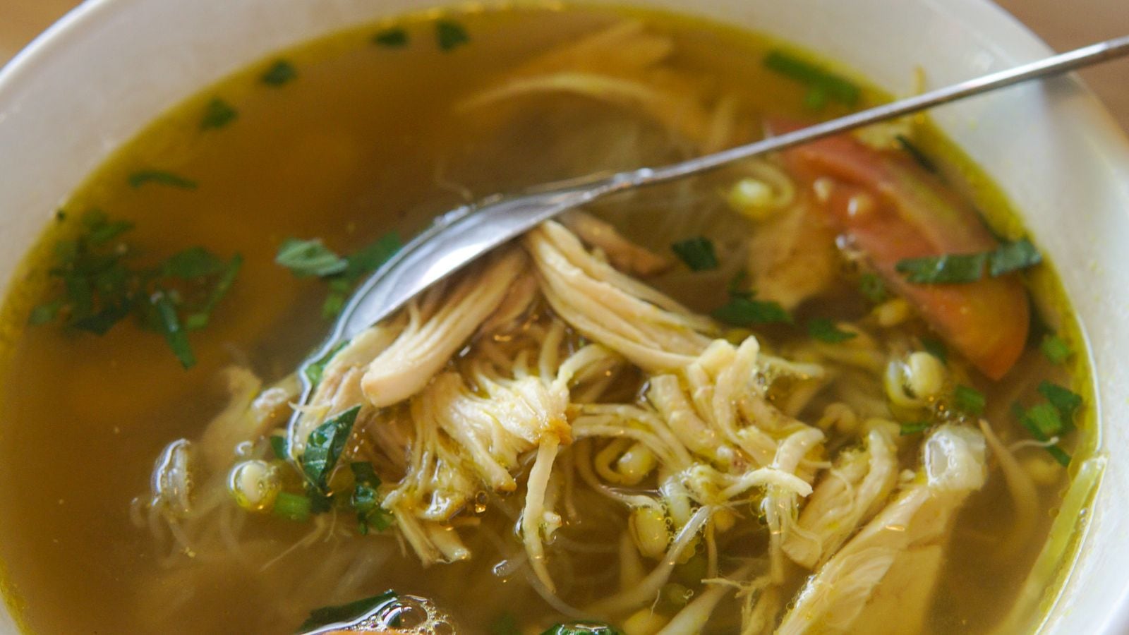 Soto ayam Indonesia dengan kuah kuning, daun segar dan tempe di mangkuk